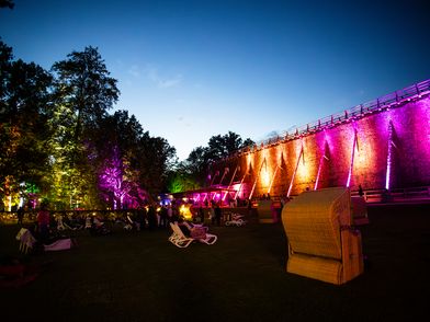 Das Gradierwerk in Bad Nauheim wird bunt angestrahlt. Im Vordergrund ist ein Strandkorb
